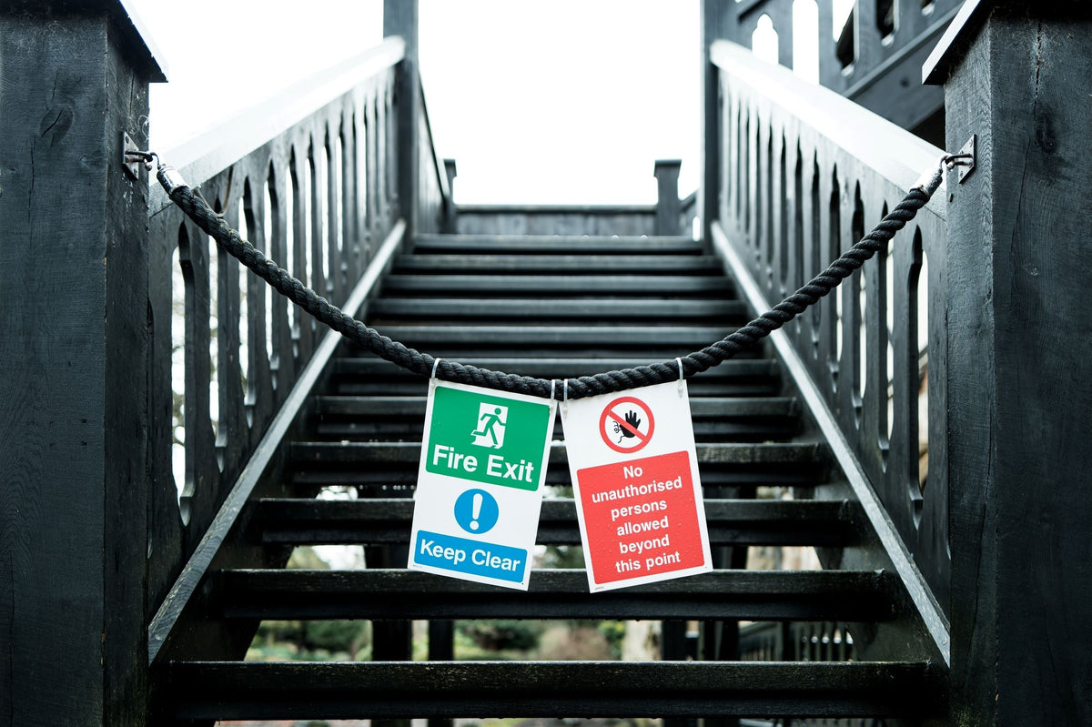 Shallow focus of warning signs and a rope barrier to exterior, wet wooden steps to the first floor of a medieval museum in the UK.